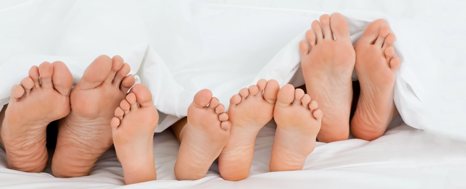 Multiple bare feet under white sheets, showing soles and toes.